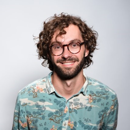 A young man with glasses and curly hair smiling
